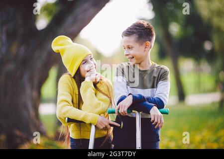 Zwei Kinder kaukasischen Jungen und Mädchen Zwillinge posieren mit Motorroller im Herbst Park. Glückliche Kinder reiten Kick Scooter im öffentlichen Park. K Stockfoto
