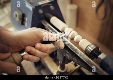 Arbeiten Sie an der Drehbank. Die Hände des Meisters mit einem Meißel in Nahaufnahme. Die Bearbeitung des hölzernen Teils. Beschäftigung und Arbeit. Stockfoto