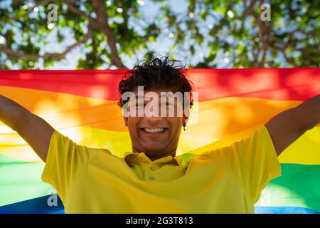 Der junge schwule Mann hält stolz die lgbt-Flagge in den Händen vor dem Meer, inklusive Stockfoto