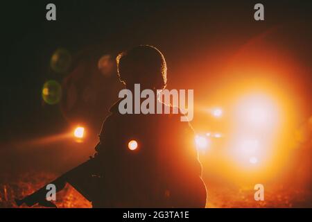 Der als Soldat der US-Infanterie des Zweiten Weltkriegs gekleidete Re-enactor hält die Maschinenwaffe in den Händen. Hochformat Mit Niedriger Taste. Licht Von Fahrzeugen Autos Lampen. Stockfoto