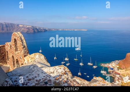 Ruinen auf Santorini und Segelkatamarane im Hafen Stockfoto