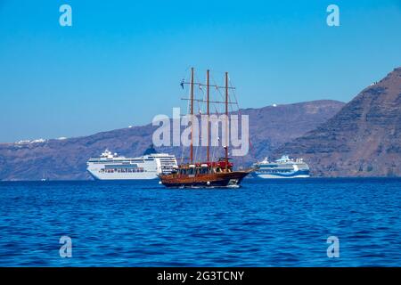 Moderne Kreuzschiffe und altes Segelschiff vor der Küste von Santorini Stockfoto