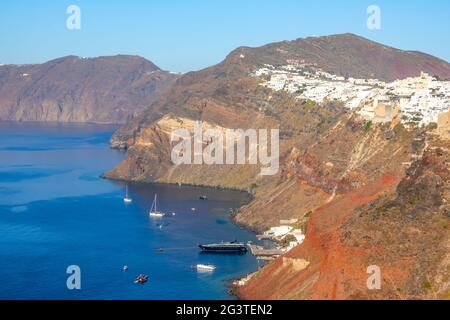 Weiße Häuser in Oia an einem sonnigen Tag und mehrere Yachten parkten in der Nähe von Santorin Stockfoto