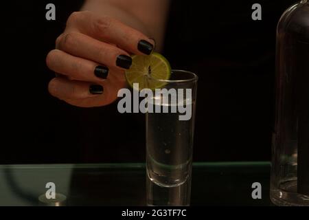 Frauenhand mit poliertem Nais, die frische Zitronenscheibe in den Mund eines Glases Tequila alchoolica-Drinks legt Stockfoto