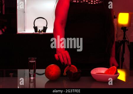 Nailpolis Hand Female richtig eine Scheibe Orange in einen Steingutkrug mit Mezcal hinter der Bar legen, wird ein Glas Whiskey mit Kopfbedeckung beobachtet Stockfoto