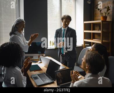 Eine Gruppe von Geschäftsleuten gratuliert zu einer Rede des Vorgesetzten, der bei der Besprechung den Computer mit schwarzem Bildschirm ansieht. Supervi Stockfoto