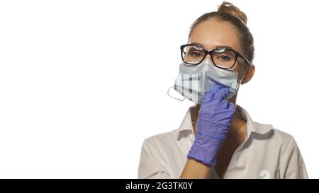 Fixing Gesicht medizinische Maske junge blonde Krankenschwester in einer Brille Blick auf die Kamera trägt weiße medizinische Uniform isoliert auf weiß Stockfoto