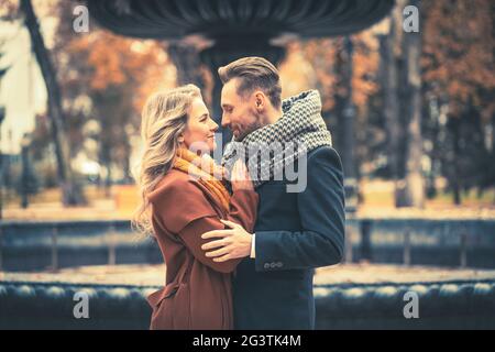 Nahaufnahme. Liebende junge Menschen, die umarmt stehen und sich in der Nähe eines alten Brunnens im Herbstpark anguchten, tragen sich Stockfoto