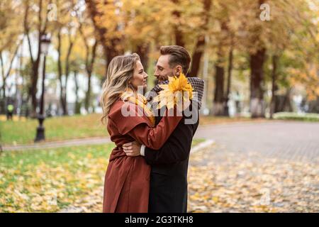 Über einen Kuss Schuss. Mann und Frau umarmten sich lächelnd und schauten sich im Herbstpark an. Außenaufnahme eines jungen Paares in l Stockfoto