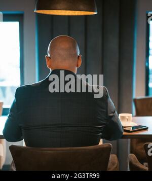 Rückansicht des CEO-Geschäftsmannes, gekleidet in teuren Anzug, sitzend am Tisch in der modernen teuren Büroeinrichtung, kahlköpfiger männlicher w Stockfoto