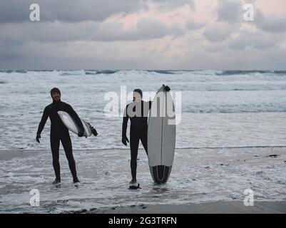 Arktische Surfer gehen nach dem Surfen am Strand vorbei Stockfoto