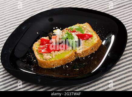 Sandwich mit Guacamole, Thunfischkonserven, Feta, Gemüse auf schwarzem Teller Stockfoto