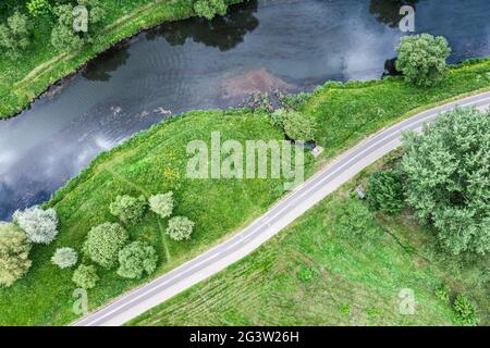 Gebogene Fahrradspur durch grüne Wiese in der Nähe des Flusses. Luftaufnahme von fliegender Drohne Stockfoto