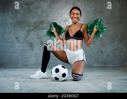 Porträt von schönen jungen lächelnden Mädchen mit grünen Cheerleader Pom-Poms und Fußball Stockfoto