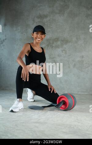 Glückliche, gesunde lächelnde Frau, die im Fitnessstudio mit dem Fitnessroller trainiert Stockfoto