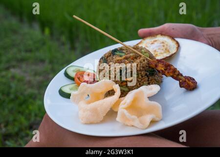 Nasi goreng, traditionelles indonesisches Gericht, serviert mit Garnelen-Crackern und Hühnersatay auf weißem Teller Stockfoto