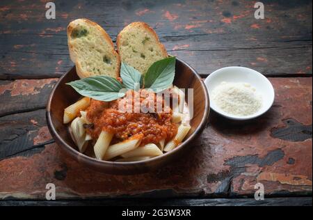 Pasta mit Tomatensauce, Knoblauchbrot und Parmesankäse auf rustikalem Holzhintergrund beiseite Stockfoto