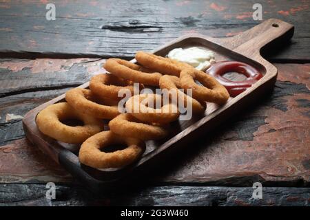 Gebratene Zwiebelringe mit Ketchup und Mayonnaise auf rustikalem Holztisch Stockfoto