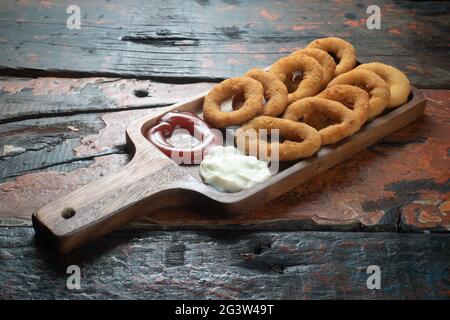 Gebratene Zwiebelringe mit Ketchup und Mayonnaise auf rustikalem Holztisch Stockfoto