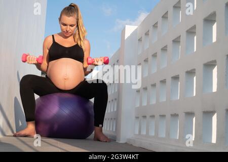 Portrait einer hübschen Schwangeren trainiert mit Fitball und Hanteln im Freien Stockfoto