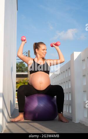 Portrait einer hübschen Schwangeren trainiert mit Fitball und Hanteln im Freien Stockfoto