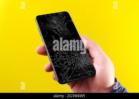 Schwarzes Smartphone mit einem defekten Touchscreen in der Hand auf gelbem Hintergrund. Stockfoto