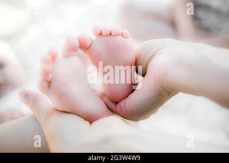 Die Mutter hält sanft die kleinen Füße ihres Babys in den Händen. Die Liebe und Gefühle eines Elternteils für sein neugeborenes Kind. Stockfoto