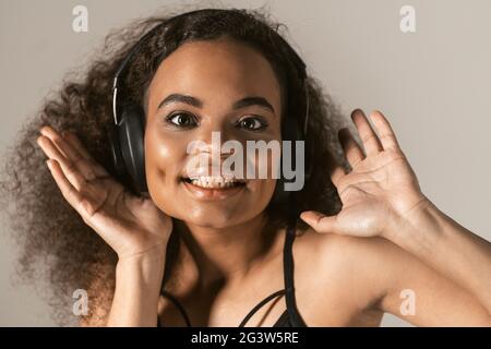 Nahaufnahme junge afroamerikanische Mädchen Musik in schwarzen Top-Kopfhörer, isoliert auf grauem Hintergrund, emotional m Stockfoto