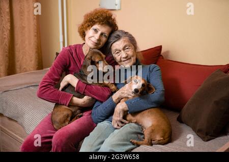 Die Erwachsene Frau kümmert sich um ihre ältere Mutter mit Demenz, verbringt Zeit zu Hause mit Eltern und Hunden, lächelt und entspannt sich glücklich Stockfoto