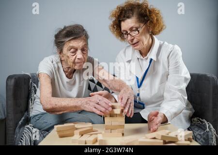 Jenga-Spiel. Thema sind Demenz, Altern und Spiele für alte Menschen. Kaukasische ältere Frau baut mit dem Hel einen Turm aus Holzblöcken Stockfoto