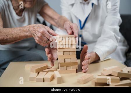 Jenga-Spiel. Thema sind Demenz, Altern und Spiele für alte Menschen. Kaukasische ältere Frau baut mit dem Hel einen Turm aus Holzblöcken Stockfoto