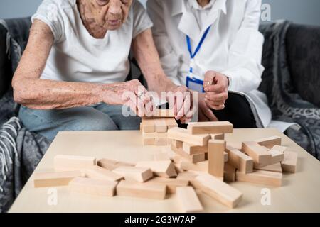 Jenga-Spiel. Thema sind Demenz, Altern und Spiele für alte Menschen. Kaukasische ältere Frau baut mit dem Hel einen Turm aus Holzblöcken Stockfoto