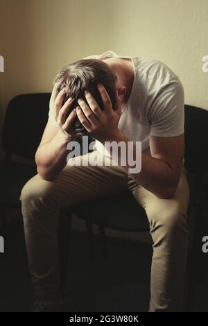 Männerprobleme. Ein junger Mann sitzt auf einem Stuhl und hält seinen Kopf in den Händen. Stockfoto