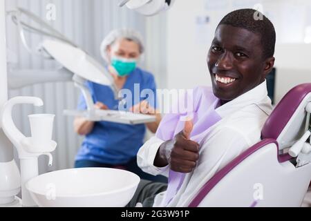 Gerne afrikanische amerikanische Mann im Behandlungsstuhl sitzen nach Zähne heilen Geben Daumen hoch Stockfoto