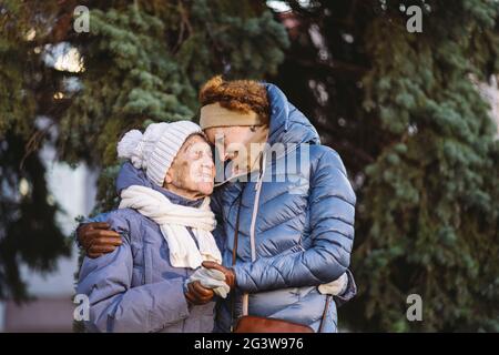 Kaukasische Frauen ältere Mutter und reife Tochter im Wintergarten auf Hintergrund Tannenbaum umarmt sich von Angesicht zu Angesicht, lächeln, sp Stockfoto