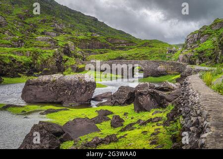 Kleine steinerne Wishing Bridge über einen gewundenen Bach in Gap of Dunloe Stockfoto