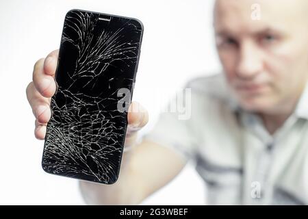 Telefon mit EINEM defekten Bildschirm Nahaufnahme. Ein weißer Mann hält ein schwarzes Smartphone mit einem geknackten Display. Stockfoto