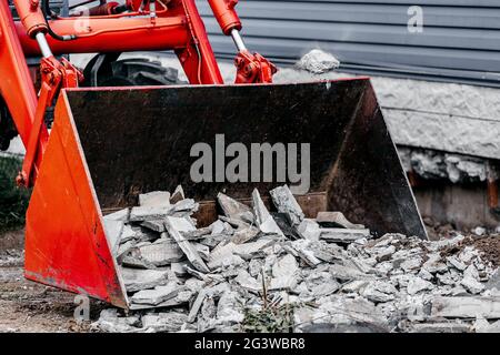 Entfernung von Bauschutt. Der Eimer des Traktors ist mit Betonschutt und Pflasterplatten gefüllt. Stockfoto