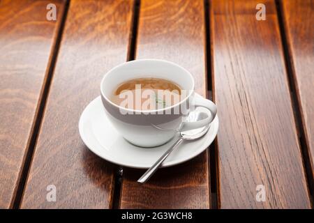 Tasse grüner Tee auf Holztisch, abendliche Entspannung. Schwarzer kräftiger Tee in einem weißen Becher. Stockfoto