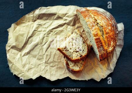 Dies ist ein Laib frisches knuspriges Brot mit Getreide auf Sauerteig. Hefe-freie hausgemachte Kuchen liegen auf gelbem Bastelpapier. Stockfoto