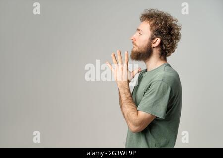 Junger, hübscher Mann, lässig seitlich, mit gefalteten Handflächen. Hübscher junger Mann mit lockigen Haaren in olivfarbenem T-Shirt und Blick auf die Kamera Stockfoto