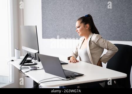 Frau, Die Rückenschmerzen Hatte, Während Sie Am Büroschalter Saß Stockfoto