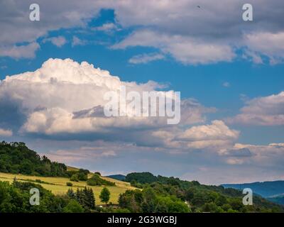 Massive Regenwolken bilden sich am blauen Himmel über hügeliger Landschaft Stockfoto