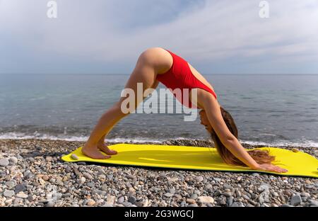 Junge Frau in rotem Badeanzug mit langen Haaren übt Dehnung Stockfoto