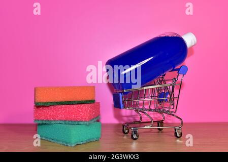 Waschschwämme und Waschmittelflasche in einem Warenkorb auf rosa Hintergrund. Haushalt für die Reinigung in der Waschküche. Housekeeping-Konzept Stockfoto