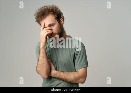 Beschämt oder Facepalm versteckt Gesicht jungen Mann bedeckt seine mit Hand Hebeln mit dem Auge, lockiges Haar in olivem T-Shirt isoliert auf weiß Stockfoto