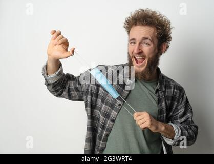 Herumspielen Spielen mit schützenden medizinischen Gesichtsmaske junger schöner Mann hält es Stretching vor dem Gesicht trägt pl Stockfoto