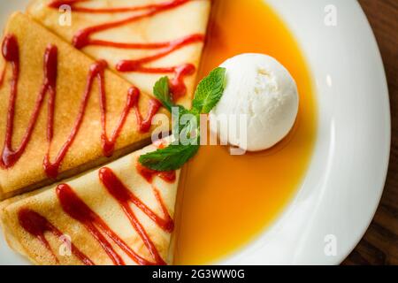 Nahaufnahme von Dessert-Pfannkuchen mit Erdbeermarmelade, Honig und einer weißen Kugel Eis. Stockfoto