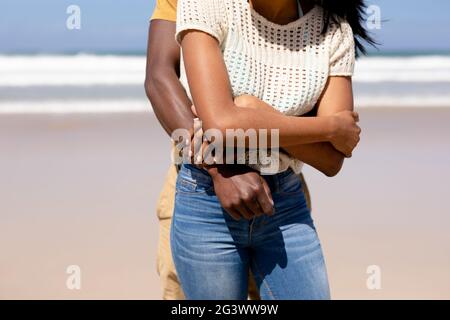 Mittelteil des afroamerikanischen Paares umarmt an einem Strand vorbei Das Meer Stockfoto