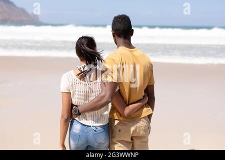 Rückansicht des afroamerikanischen Paares, das sich an einem Strand umarmt Blick auf das Meer Stockfoto